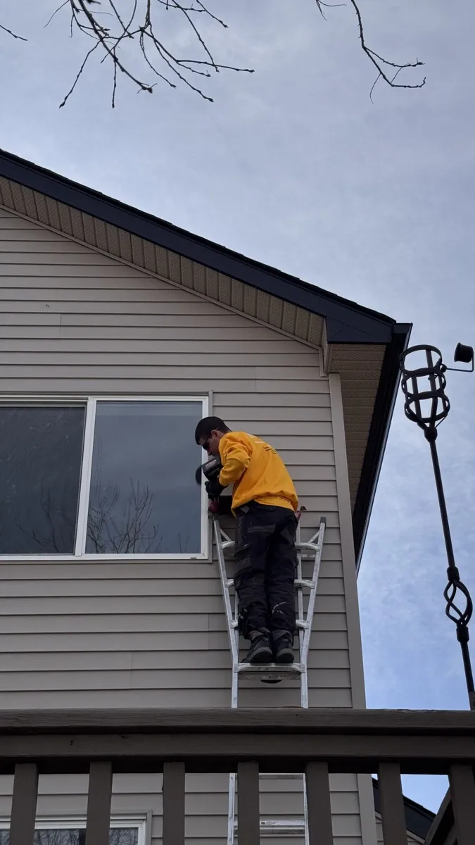 Value Windows installer working on a second-floor window on an overcast Alberta day